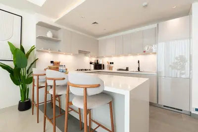 a kitchen with white cabinets and bar stools at Luxury 3BR Skyline Apartment - Sobha The Crest Dubai in Dubai