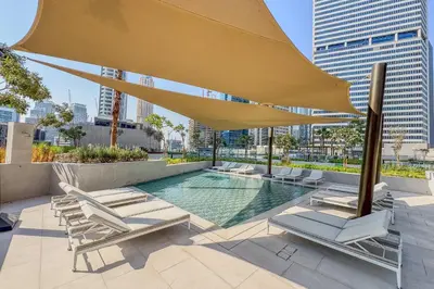a pool with chairs and a large yellow umbrella at Elevated 2 Bedroom with Khalifa view in Peninsula in Dubai