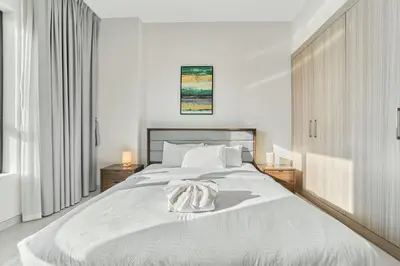 a white bedroom with a large bed with white sheets at Chic 1BR Getaway in Tulip Oasis 9 Majan in Dubai