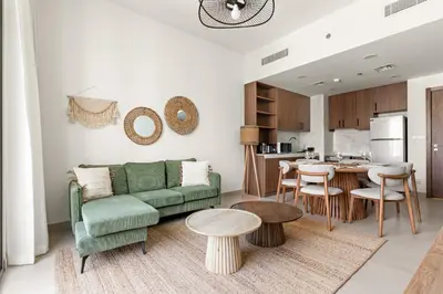 a living room with a green couch and a kitchen at VayK - Chic 2BR in Town Square with Pool View in Dubai