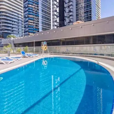 a large blue swimming pool with chairs and buildings at Heart of Downtown Luxury 1BHK Dunya in Dubai