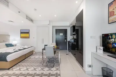 a bedroom with a bed and a desk and a kitchen at Stylish Stay at DAMAC Maison Cour Jardin Canalview in Dubai