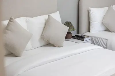 a white bed with white pillows on top of it at Brand New Building! 2 Double Bed! Ideal Location with 5-star Pool and Gym! in Dubai
