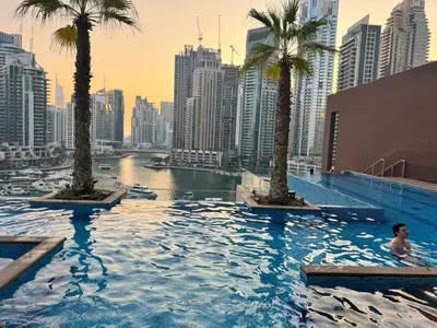 a man in a swimming pool with palm trees in a city at Free Infiniti Pool and Jacuzzi - Marina Gate Luxury Stay - Enjoy Dubai Marina Views in Dubai