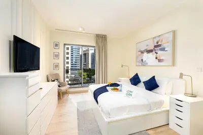 a white bedroom with a bed and a tv at South Ridge By Luxe Living - Full Burj Khalifa View in Dubai
