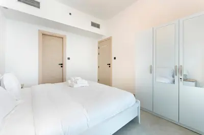 a white bedroom with a bed and a closet at Modern 1BR with Pool & Gym, Burj Khalifa View, Al Jaddaf in Dubai