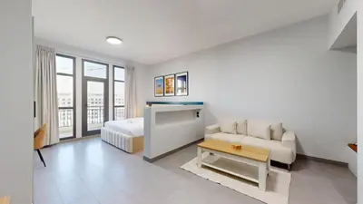 a white room with a bed and a couch and a table at Vacationer I Modern Studio I Pool & Gym Access I 5-min Drive to Miracle Garden I Arjan in Dubai