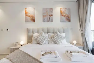 a bedroom with a large white bed with three paintings on the wall at Highest Infinity Pool - Paramount Midtown Hotel & Luxury Apartments Burj Khalifa view & Partial Fountain View in Dubai