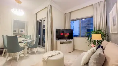 a living room with a television and a table with chairs at Damac Maison Downtown Dubai Luxury 1BR Walk to Dubai Mall in Dubai