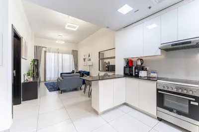 a kitchen with white cabinets and a living room at HAVN - 1 bedroom in The Wings, Arjan in Dubai