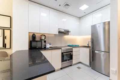 a kitchen with white cabinets and a stainless steel refrigerator at HAVN - 1 bedroom in The Wings, Arjan in Dubai