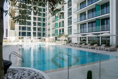 a swimming pool with chairs and umbrellas next to a building at Radiant Studio in Binghatti Azure with Pool & Gym in Dubai