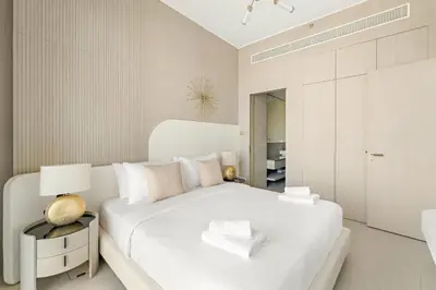 a white bedroom with a large white bed and a table at VayK - Modern & Elegant 1BD in JVC in Dubai