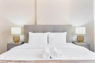 a bedroom with a bed with two lamps and white slippers at Sunny & Stylish 1Bed 7-Min Walk to the Beach! in Dubai