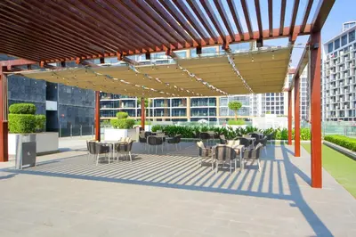 a patio with tables and chairs under a wooden pergola at Silk Valley - Luxury St with Pool Access & Balcony | 10 Min to Downtown in Dubai