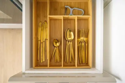a wooden cabinet with goldoons and forks and knives at La Mer Le Pont 1 Bedroom Beachside Apartment in Dubai