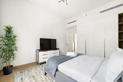 a white bedroom with a bed and a tv at La Mer Le Pont 1 Bedroom Beachside Apartment in Dubai