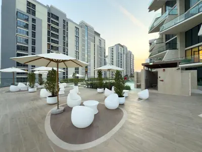 a patio with white chairs and umbrellas on a building at Private Pool - Amazing 1BR Apartment in JVC in Dubai