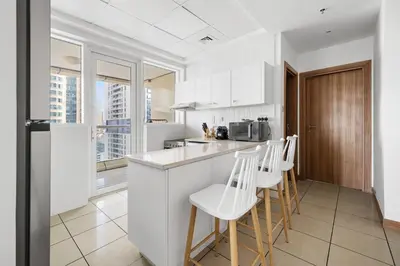 a kitchen with white cabinets and white stools at Modern 1BR in Dubai Marina with Balcony Gym & Pool in Dubai
