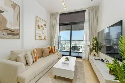 a living room with a couch and a large window at Located Near Community Parks, Convenient Stores, an RTA Bus Stop, And Just Minutes From The Mall - Binghatti Emerald, JVC by Deluxe Holiday Homes in Dubai