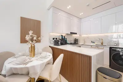 a white kitchen with a table and chairs and a counter at Close to Community Park, Minutes Walk from Circle Mall, and Short Drive to Dubai Miracle Garden and Butterfly Garden - Binghatti Amber, JVC by Deluxe Holiday Homes in Dubai
