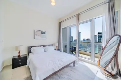 a white bedroom with a bed and a large window at Spacious 1BHK Apt with Canal View in Dubai Marina in Dubai