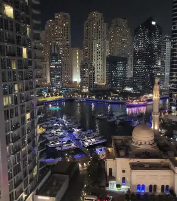 a view of a city at night with boats in a harbor at Luxury 1BR Apt with water canal & Marina View in Dubai