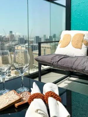a balcony with a chair and wine glasses and a window at Luxe Studio Perch in Binghatti Azure with Pool & Gym in Dubai
