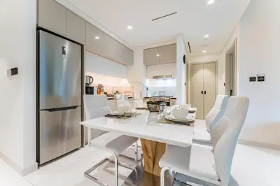 a white kitchen with a dining table and white chairs at Steps Away From JBR Beach And Marina Promenade, Quick Access To Palm Jumeirah, Surrounded by Leisure And Entertainment Hubs - Marina Vista Tower 2, Emaar Beachfront by Deluxe Holiday Homes in Dubai