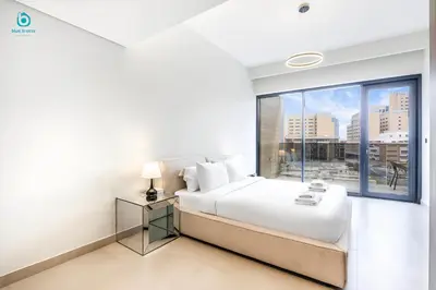 a white bedroom with a bed and a large window at Blue Breeze Cozy 1 BR in JVC Al Serh Residence 11 in Dubai