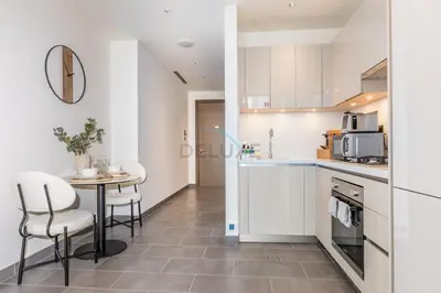 a kitchen with white cabinets and a table and chairs at Located Few Minutes Drive to Downtown Dubai, Burj Khalifa and Dubai Mall, Surrounded by Lush Green Community - Sobha Hartland The Crest Tower C by Deluxe Holiday Homes in Dubai