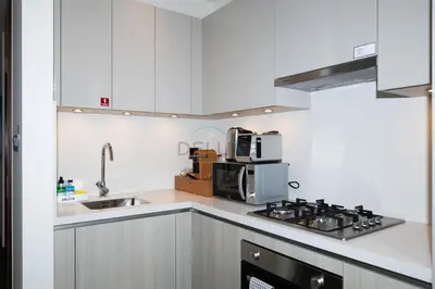 a white kitchen with a stove and a microwave at Located Few Minutes Drive to Downtown Dubai, Burj Khalifa and Dubai Mall, Surrounded by Lush Green Community - Sobha Hartland The Crest Tower C by Deluxe Holiday Homes in Dubai