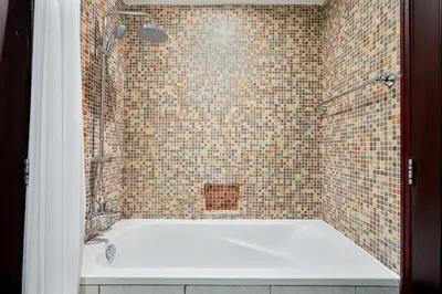 a bathroom with a tub with a tiled wall at Charming Oasis Near Dubai Mall & Burj Khalifa in Dubai
