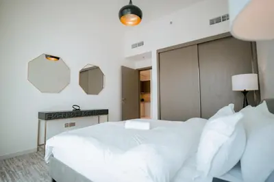 a white bedroom with a large white bed and a desk at Cozy Apartment with Private Beach & Palm Views in Dubai
