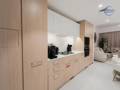 a kitchen with wooden cabinets and a living room at Premium 1 Bedroom Stay in Berkeley Place in Dubai