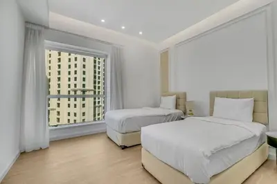 two beds in a white room with a window at Sadaf 2701 in Dubai