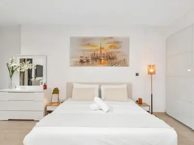 a white bedroom with a large white bed and a painting at JBR Studio - Steps to Beach & Marina Walk - Pool & Gym in Dubai