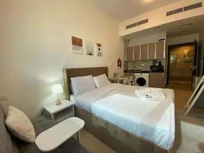 a bedroom with a bed and a chair and a kitchen at Charming Studio Apartment in Jadaf in Dubai