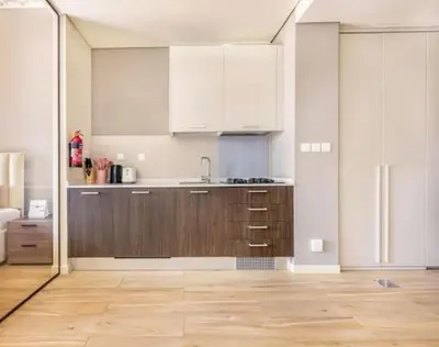a kitchen with white cabinets and a wooden floor at Luxurious cozy studio in Dubai