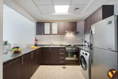 a kitchen with wooden cabinets and a refrigerator at Vogue Arjan Siraj Tower near Miracle Garden and Dubai Hills Mall, One Bedroom Apartment with Large Balcony and City View, Access to all Amenities in Dubai