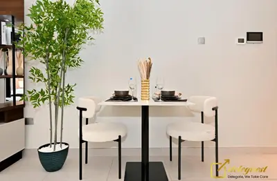 a dining room table with white chairs and a plant at Stylish Studio with City Views in Dubai Hills in Dubai