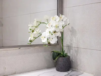 a vase of white flowers sitting on a counter next to a mirror at Livin' Holidays - Studio - Azizi Lovely Studio in Dubai