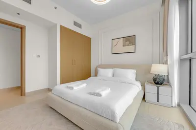 a white bedroom with a large bed and a lamp at Neat 3BR Habour Views with Balcony-Burj Khalifa View, Pool, Gym and Modern Facilities in Dubai