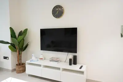 a white entertainment center with a tv and a clock on a wall at 2BR Luxury, 2,5 bath, Baby bed, Gym & Pool in Dubai