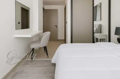 a white bedroom with a white bed and a chair at Cozy 1-Bedroom Flat in Central JVC in Dubai
