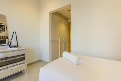 a bedroom with a white bed and a dresser at Balcony-Facing Pool 2BR with Assistant Room, Minutes Walk to Park, Miracle and Butterfly Garden, Divine Living, Arjan by Deluxe Holiday Homes in Dubai