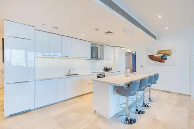 a kitchen with white cabinets and a island with bar stools at Palm Home next to Nakheel Mall with Private Beach in Dubai