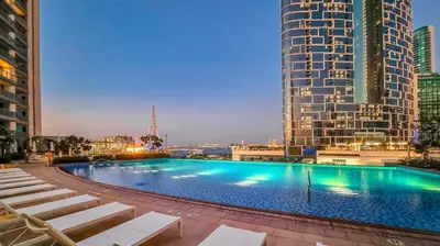 a large swimming pool with chairs and a tall building at Luxury Bluewater Escape 1BR Canal view 5242T in Dubai
