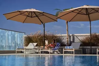 a woman sitting in a chair next to a pool at Vogue JVT Novotel near Springs Souk Mall, One Bedroom apartment with Balcony and Vibrant Community View, Access to all Amenities in Dubai