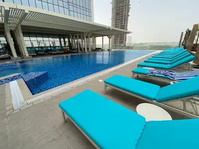 a pool with blue lounge chairs in front of a building at Vogue JVT Novotel near Springs Souk Mall, Studio Apartment with Balcony and City View, Access to all Amenities in Dubai